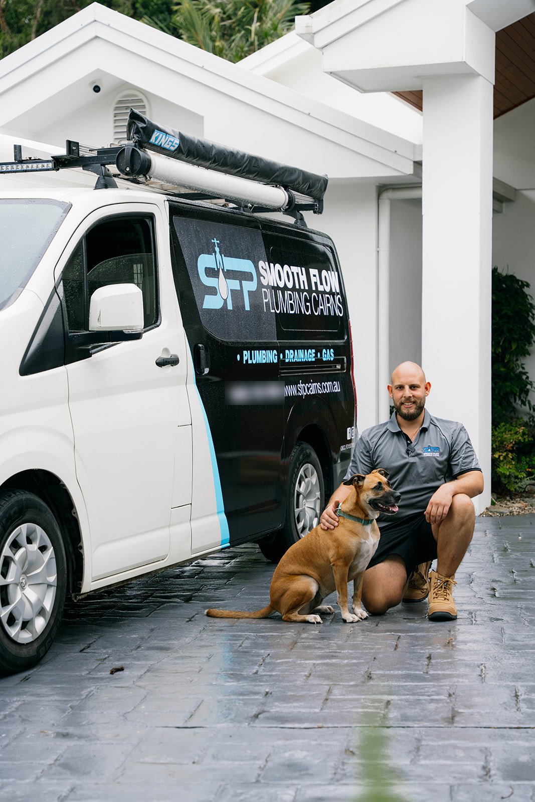 Harris from Smooth Flow Plumbing crouched beside the van with Luna the dog